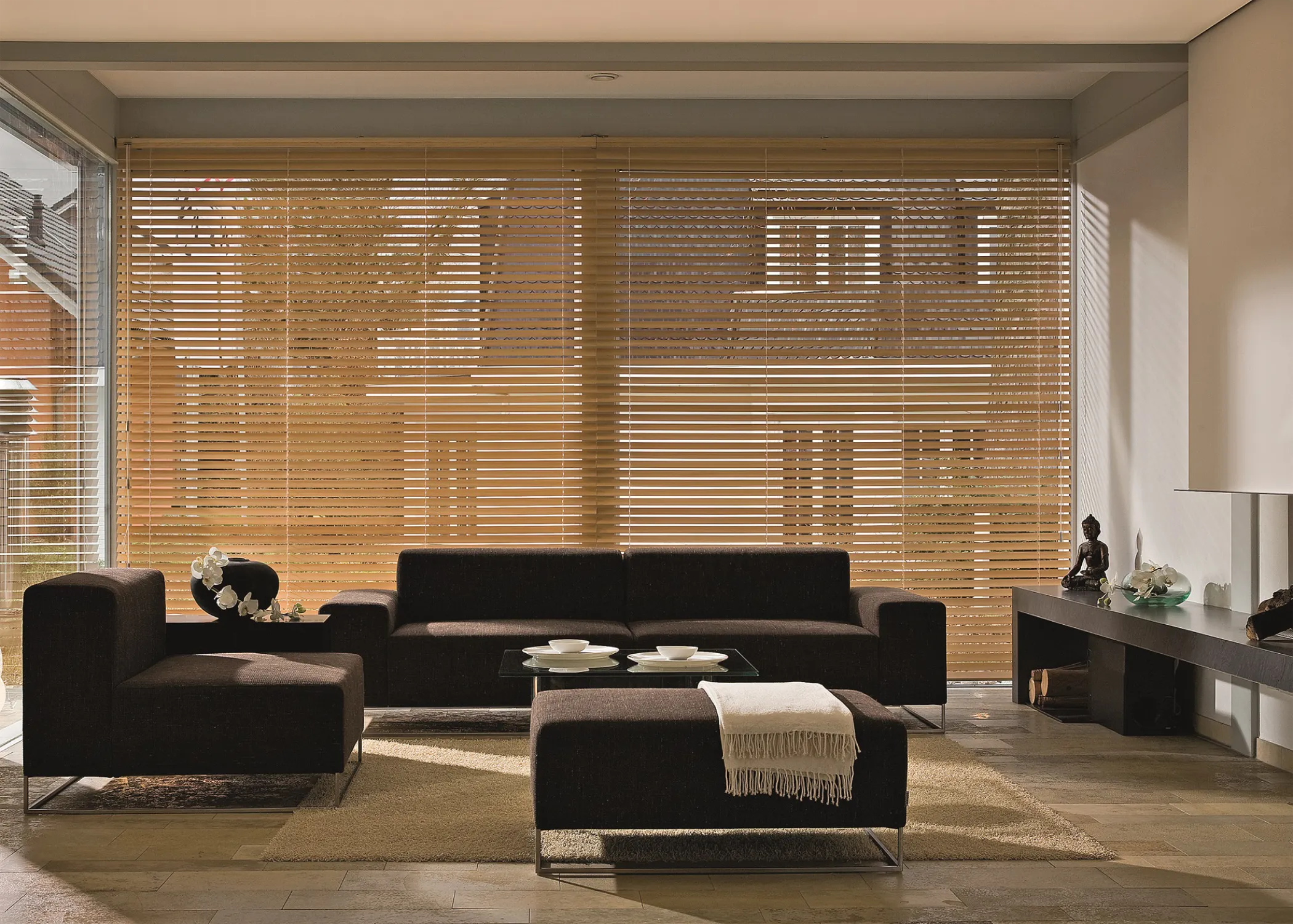 Fenster mit Holz-Jalousie verdunkelt und im Vordergrund eine Sofa-Sitzgruppe.