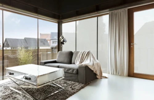 Eine Wohnzimmer mit einer Eckfront aus Glas. Eine Hälfte der Fenster ist mit einer Folie beschichtet. Die das hineinschauen verhindert.