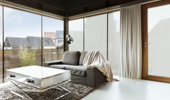 Eine Wohnzimmer mit einer Eckfront aus Glas. Eine Hälfte der Fenster ist mit einer Folie beschichtet. Die das hineinschauen verhindert.