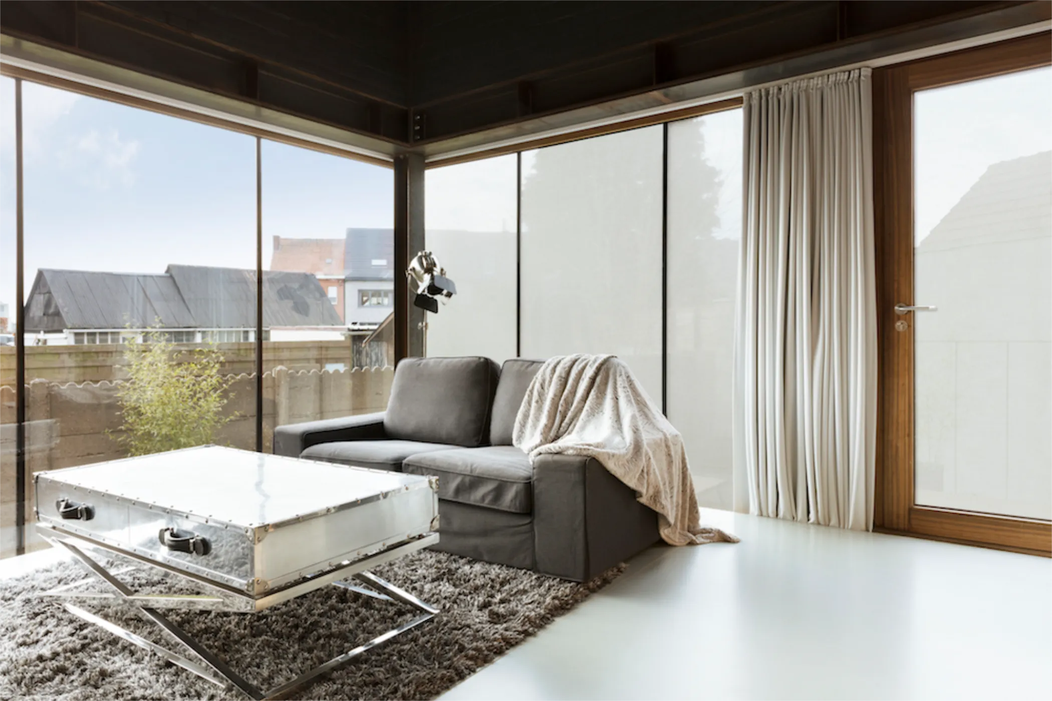 Eine Wohnzimmer mit einer Eckfront aus Glas. Eine Hälfte der Fenster ist mit einer Folie beschichtet. Die das hineinschauen verhindert.