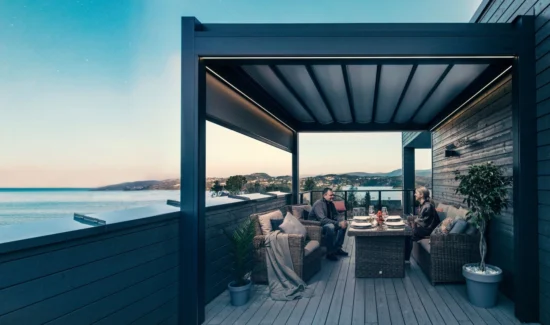 Ein Mann und eine Frau sitzen auf einem Balkon am Meer, überdacht von dem Textildach Brustor B300.