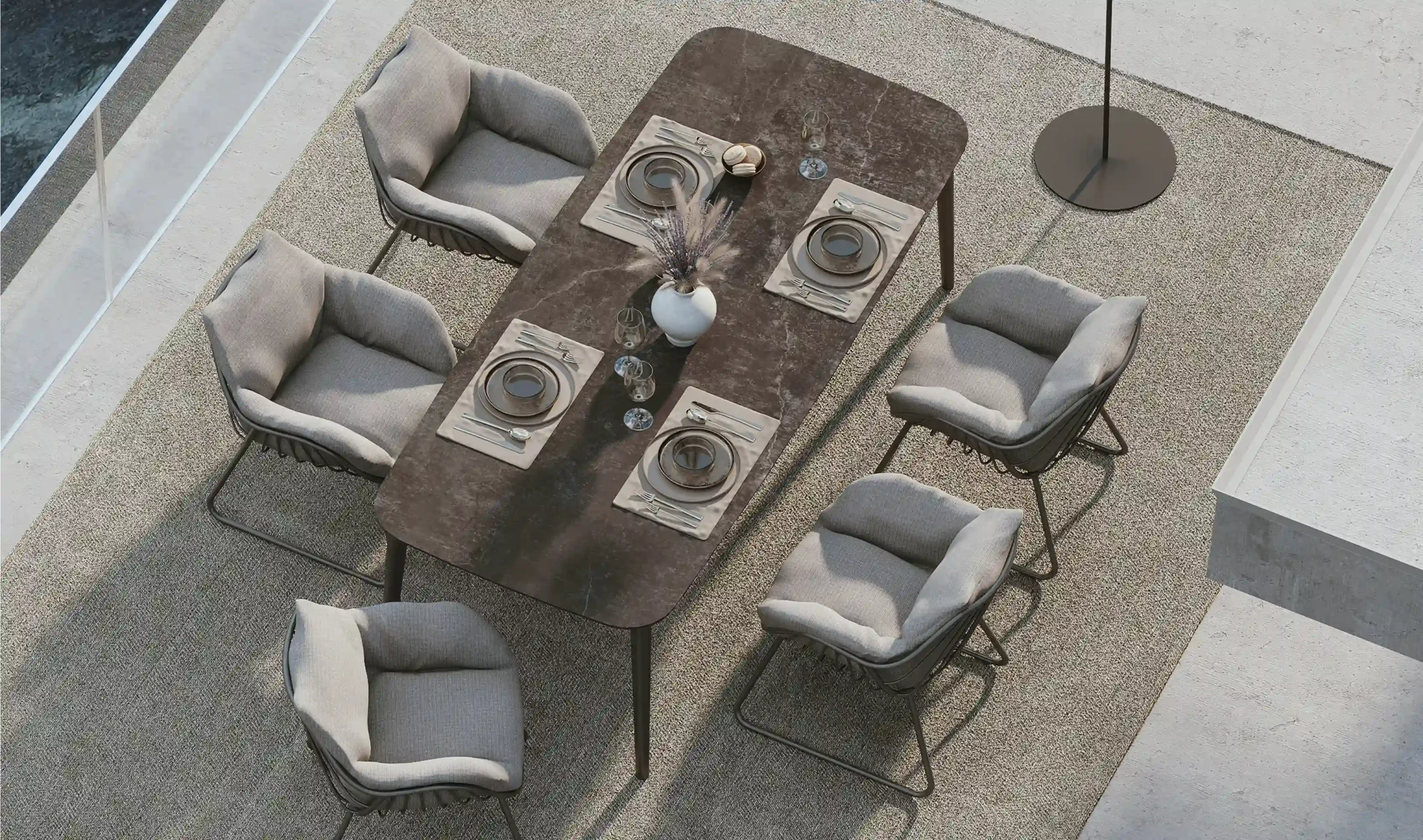 Aufeinander abgestimmt stehen ein CHARLIE Esstisch und fünf CHILL Diningsessel gepolstert mit einem Teppisch auf einem Balkon. Beide Terrassenmöbel werden von Solpuri hergestellt.