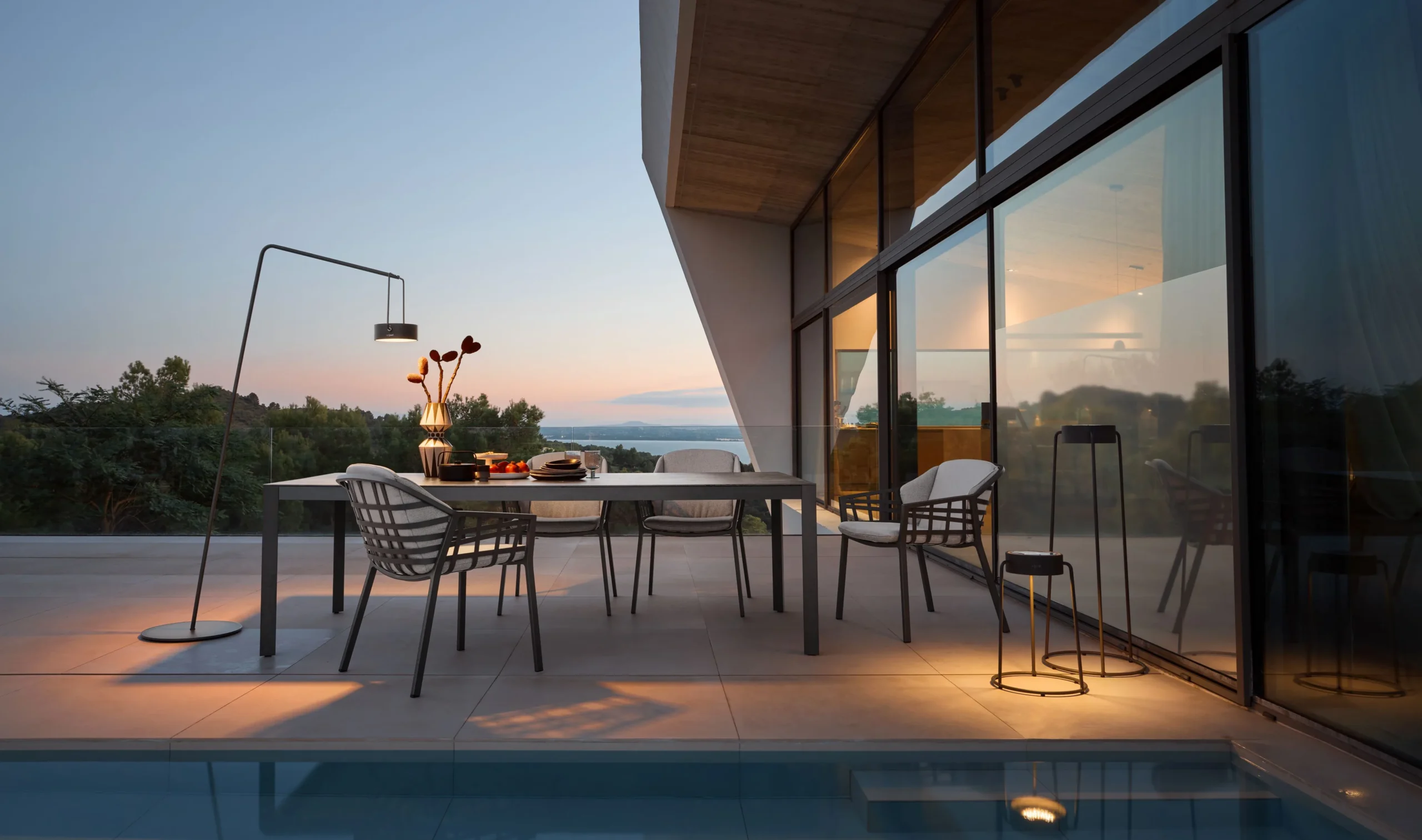 Einige Terrassenmöbel der Marke Solpuri werden nach Sonnenuntergang mit Outdoor-Lampen beleuchtet. Kombiniert werden dabei ein CLASSIC Esstisch mit BASKET Dining Sesseln.