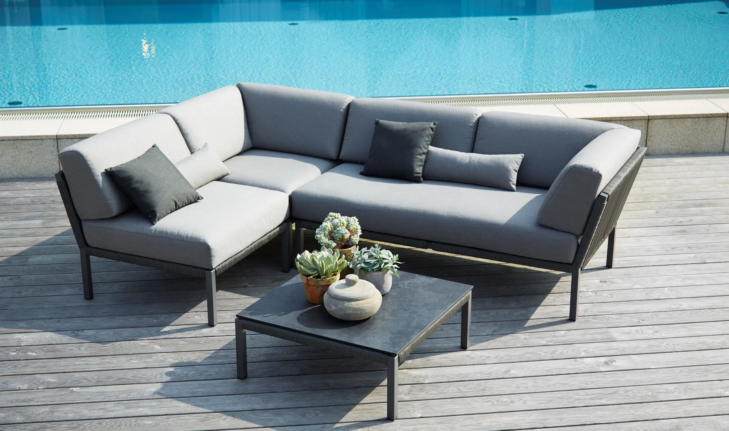 Die CLUB Lounge von Solpuri Terrassenmöbel auf einem Holzdeck vor einem Pool.