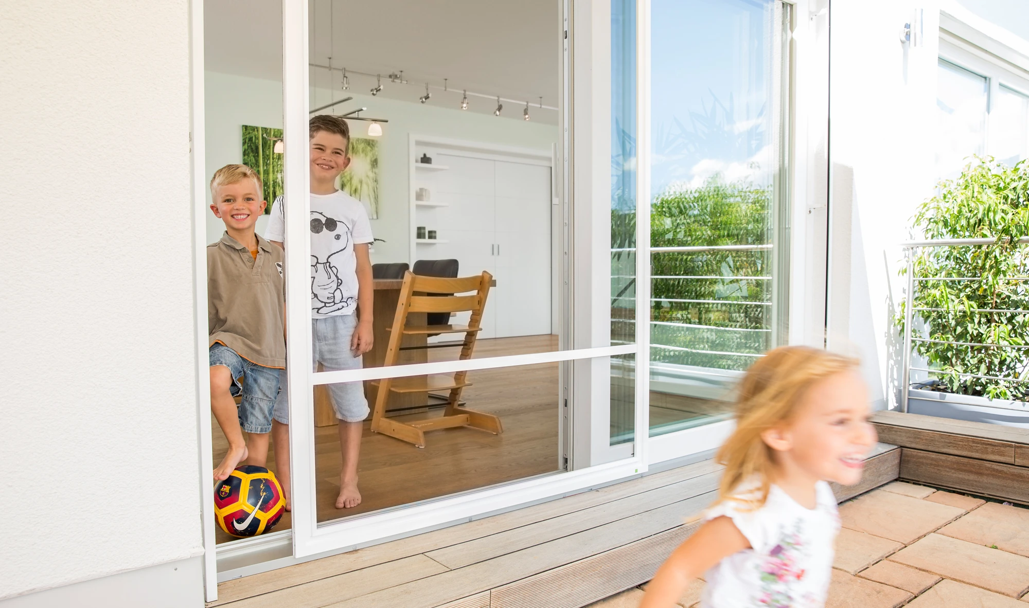 Kinder auf dem Weg zum Spielen in den Garten, wobei die geöffnete Tür durch ein Insektengitter geschützt wird.