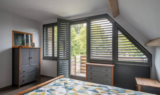 Schwarze Shutters in einem Schlafzimmer mit geöffeter Balkontür.