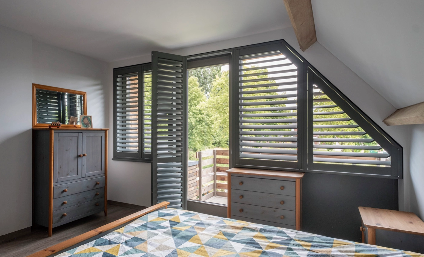 Schwarze Shutters in einem Schlafzimmer mit geöffeter Balkontür.
