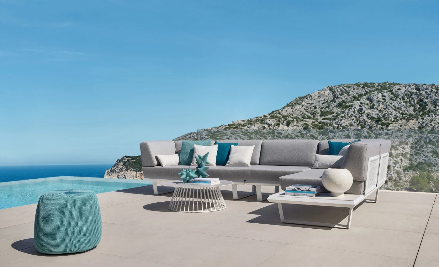 Lounge "BOOM" der Terrassenmöbel von Solpuri mit Beistelltisch neben einem Pool vor Meer und Berg.
