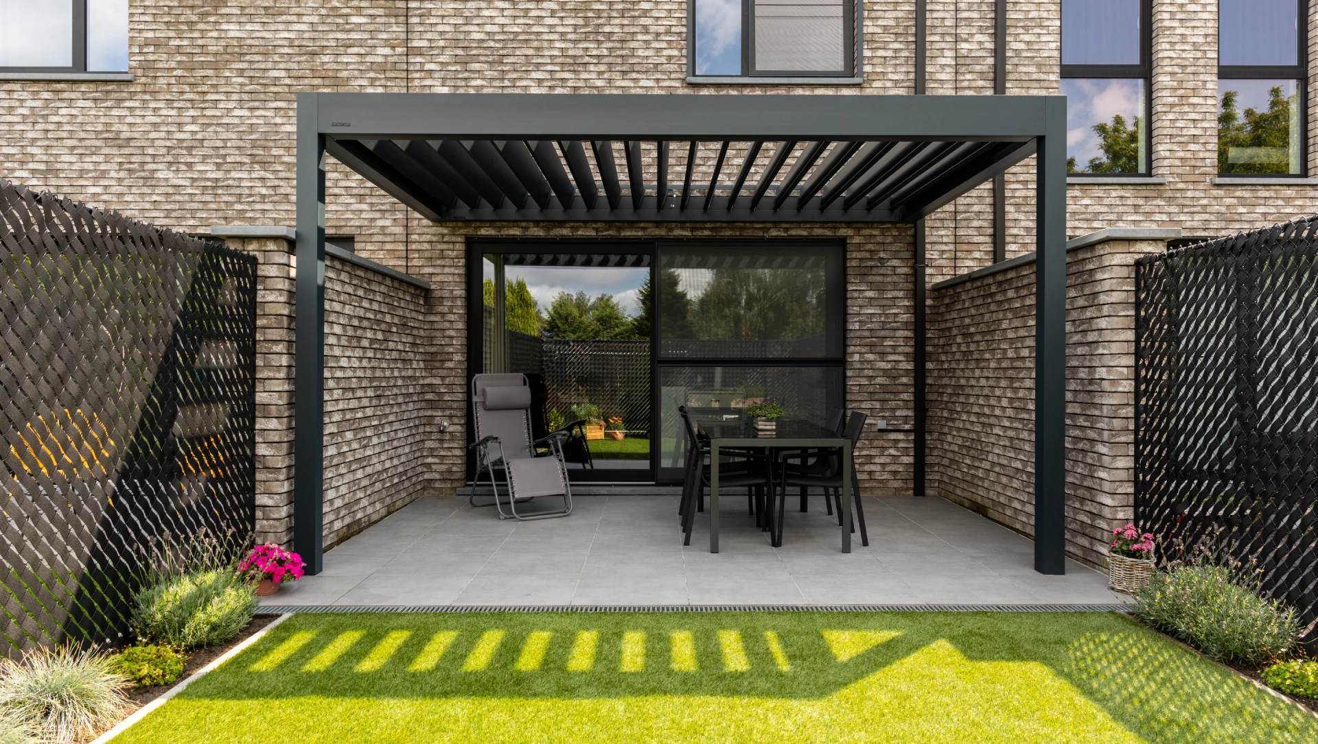 Das Lamellendach Brustor B160 XL angebaut an eine Hauswand.