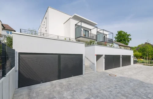 Sechs Garagen ausgestattet mit dunkelfarbenen ROMA Garagentoren vor einem Mehrfamilienhaus.