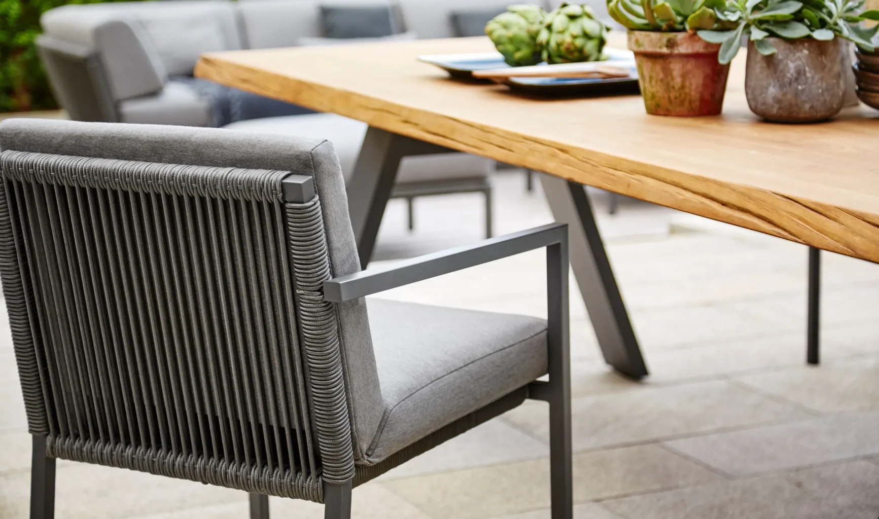 Die Gartenmöbel TIMBER Esstisch und ein CLUB Dining Sessel von Solpuri im Vordergrund.