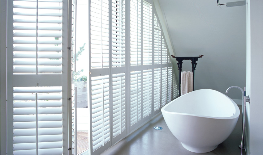 Shutters in einem Badezimmer neben einer Badewanne, leicht geöffnet.