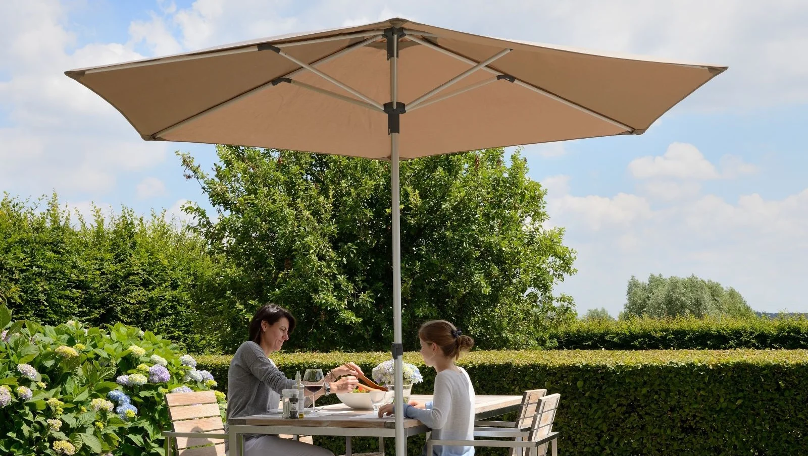 Eine Mutter mit Tochter beim Essen an einem Tisch im Freien unter einem Prostor P2 Sonnenschirm.