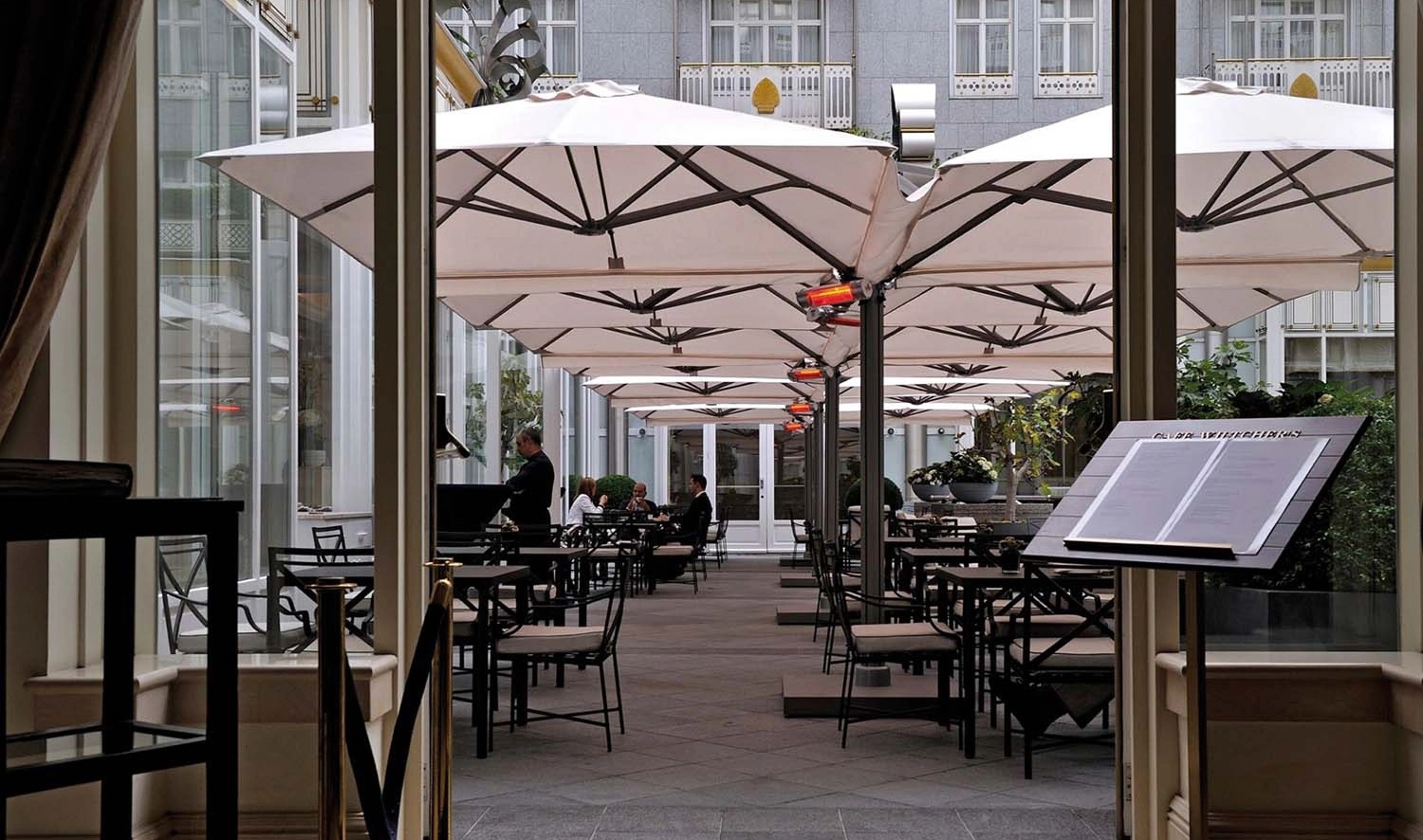 Eine Reihe von Prostor P6 Multimasten über dem Außenbereich eines Gastronomiebetriebs. Die Schirme sind mit Heizstrahlern ausgestattet.