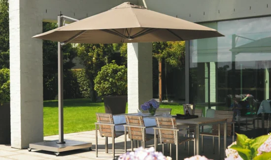 Ein Prostor P7 Sonnenschirm in bräunlicher Farbe über einem Esstisch auf der Terrasse eines modernen Hauses mit Garten.