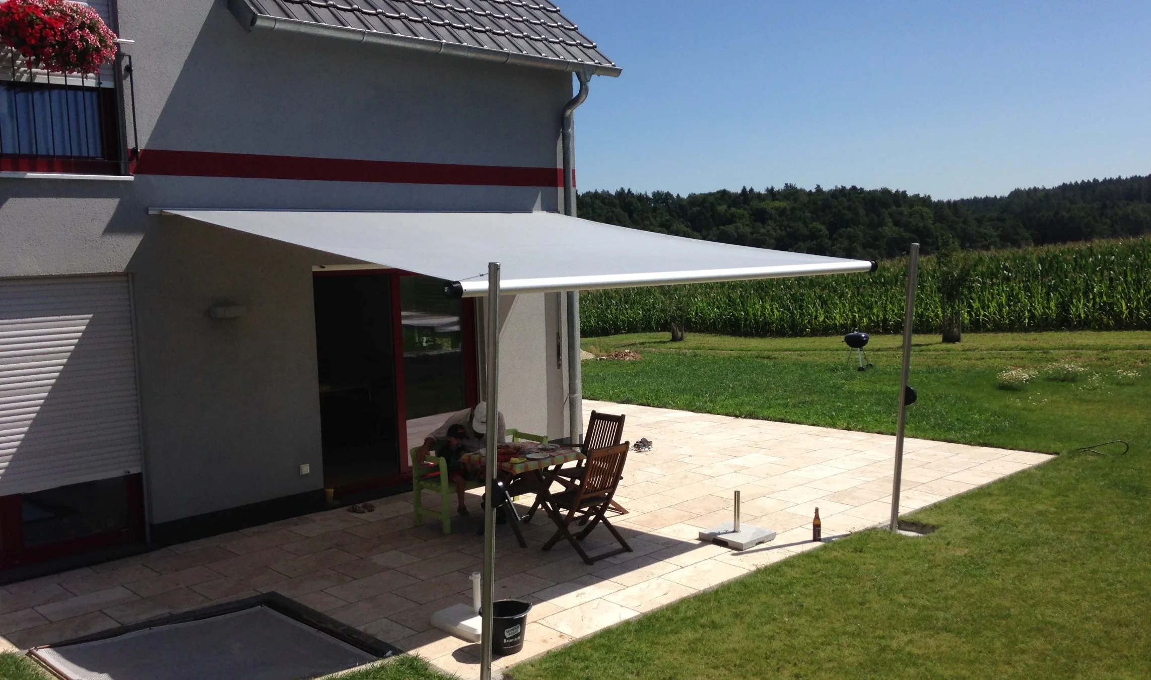 Ein kleiner eckiger Tisch wird durch ein Shadesign SHADE INOX vor der Sonne geschützt.