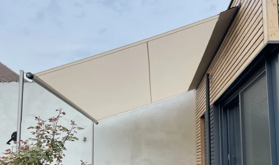 Seitenansicht eines hellen SHADE INOX Sonnensegels, schräg aufgespannt über Sitzgelegenheiten auf einer Terrasse.