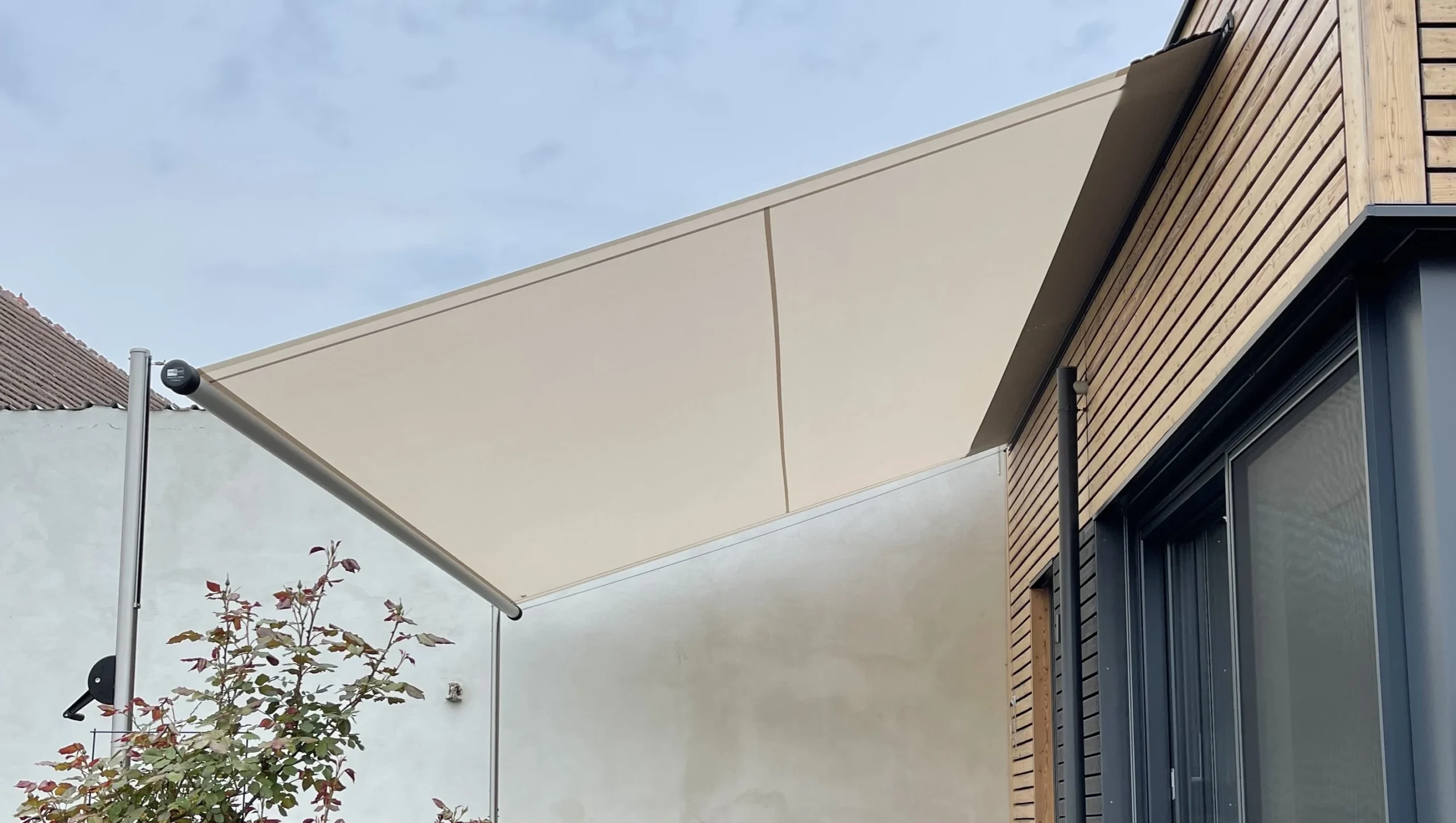 Seitenansicht eines hellen SHADE INOX Sonnensegels, schräg aufgespannt über Sitzgelegenheiten auf einer Terrasse.