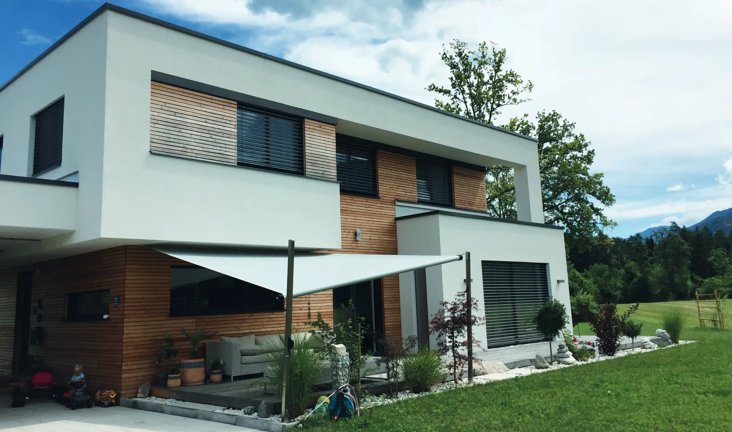 Ein modernes Haus mit einem schräg gespannten SHADE INOX Sonnensegel zu Beschattung eines Outdoor-Sofas.