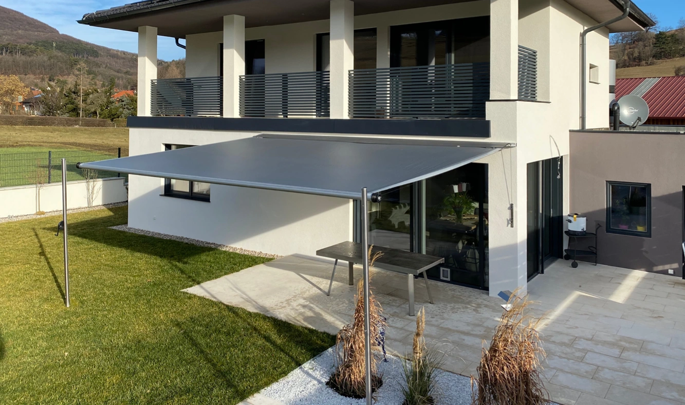 Ein dunkles Sonnensegel SHADE INOX ist über Terrasse und Wiese aufgespannt.