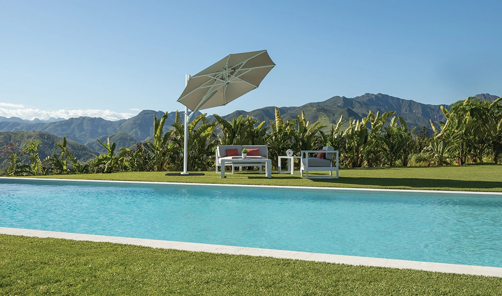 Sitzgelegenheiten mit Tisch neben einem Pool mit einem runden Shademaker Solaris schräg eingestellt für optimalen Schattenwurf.