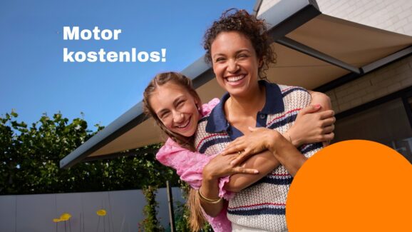 Ein Mädchen umarmt seine Mutter von hinten. Beide sehen den Betrachter lächelnd an. Im Hintergrund ist blauer Himmel zu sehen. Darauf steht: Motor kostenlos! Rechts davon im Hintergrund ist eine ausgefahrene sandfarbene Markise mit anthrazitfarbenem Gestell zu sehen. Am vorderen rechten Bildrand ist ein orangefarbener Kreis im Anschnitt zu sehen.