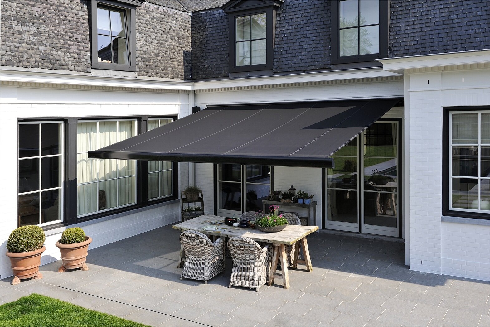 eine schwarze Markise ist auf einer Terrasse über dem Esstisch ausgefahren