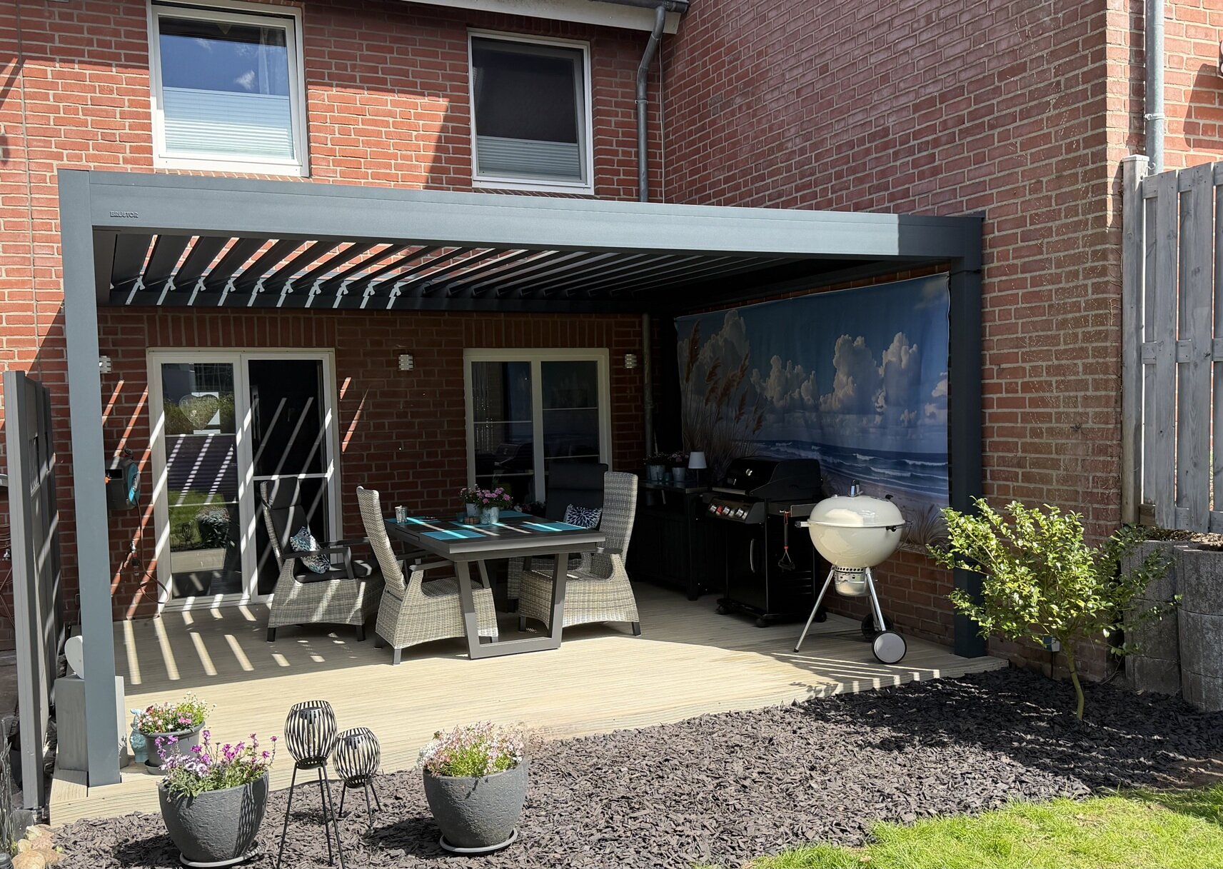 Ein Lamellendach in anthrazit als Überdachung über einer Terrasse mit Tisch und Stühlen.