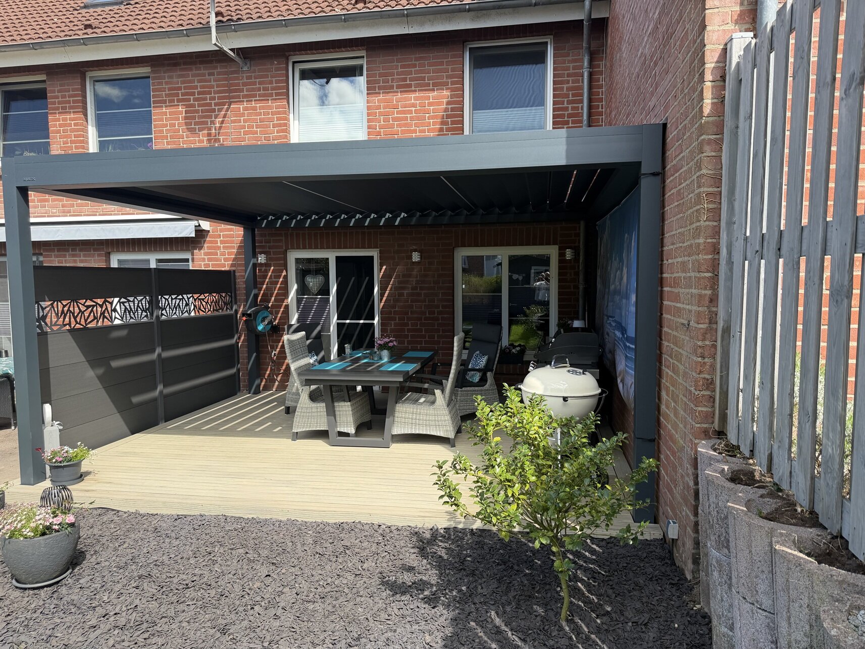 Ein Lamellendach wird von vorne gezeigt. Es ist an eine Hausfassade angeschlossen und über dacht eine Terrasse.