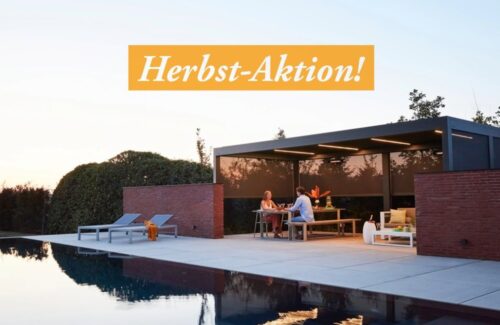 Ein Paar sitzt unter einem beleuchteten Lamellendach mit heruntergefahrenen seitlichen Screens. Im Vordergrund ist ein Pool zu sehen.